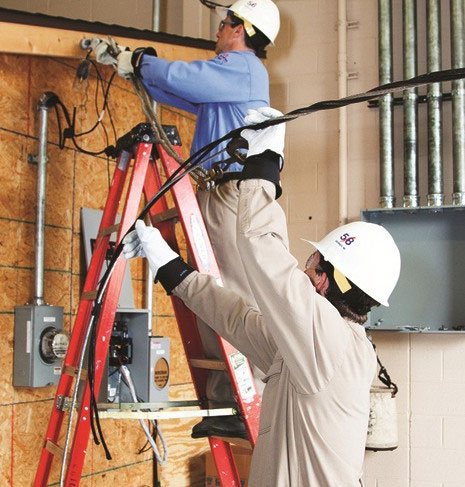 Two men working on a wall with electrical wires.