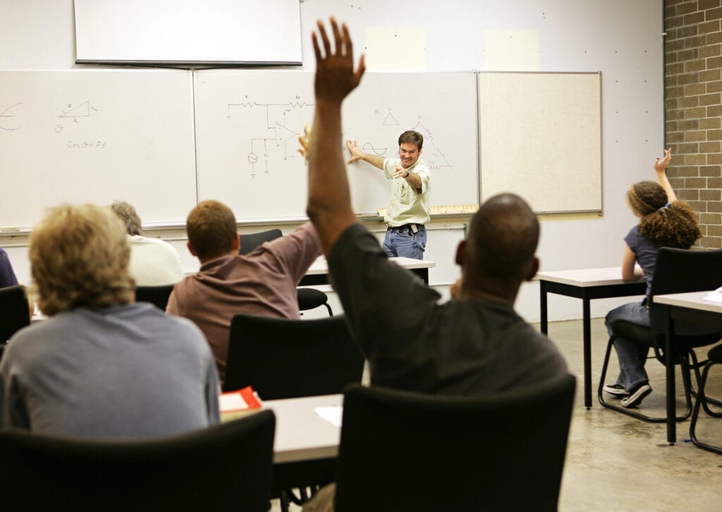 A man raising his hand in front of a class.